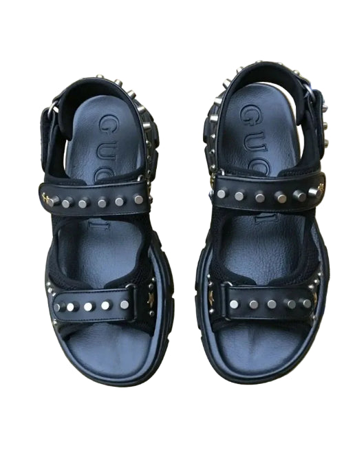 Black studded sandals on a floral-patterned fabric background
