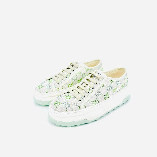 A pair of Gucci low-top sneakers featuring a white canvas upper with a green GG monogram pattern, white laces, and a chunky white platform sole with a light mint green tint.