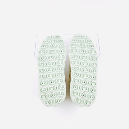A pair of light mint green non-slip rubberized shoe soles shown from the bottom, featuring a grid of circular textured grips, displayed on a clear stand against a white background.