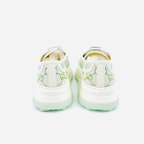 A pair of Gucci low-top sneakers shown from the back, featuring a white canvas upper with the signature green GG monogram pattern and thick white platform soles with a light mint green tint.