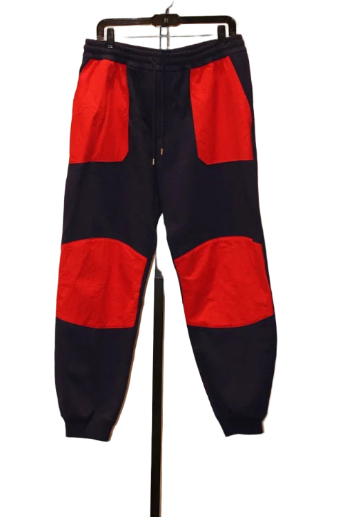 Navy and red jogger pants on a hanger against a neutral wall.