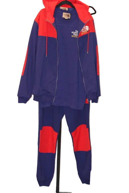 Navy and red tracksuit with The North Face logo on a hanger against a white wall.