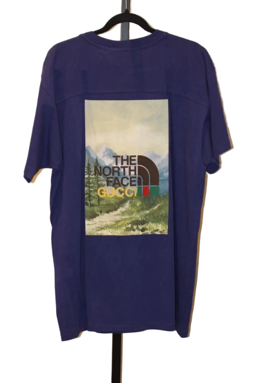 Purple t-shirt with 'The North Face' and 'Gucci' logos on a hanger against a white wall.