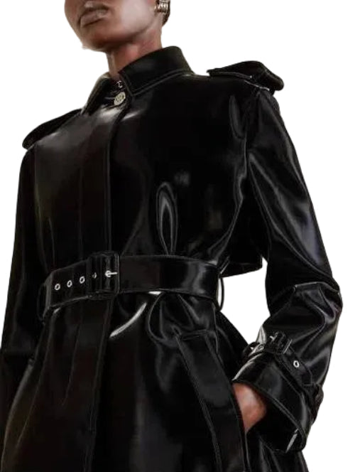 A close-up of a person wearing a dark, structured coat or jacket with a wide collar and a belted waist, shown against a dark background.