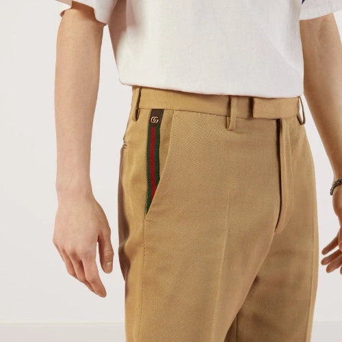 A close-up of a person wearing tan chinos with a signature green and red web stripe detail on the side pocket, paired with a white t-shirt.