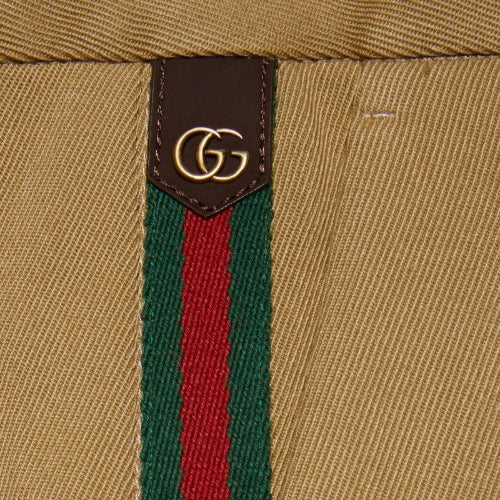 Close-up of a beige woven textile with a vertical green and red stripe and a brown rectangular patch featuring a gold interlocking GG logo.