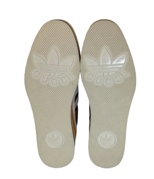 A pair of beige slip-on shoes with a circular logo printed on the sole, shown against a plain white background.