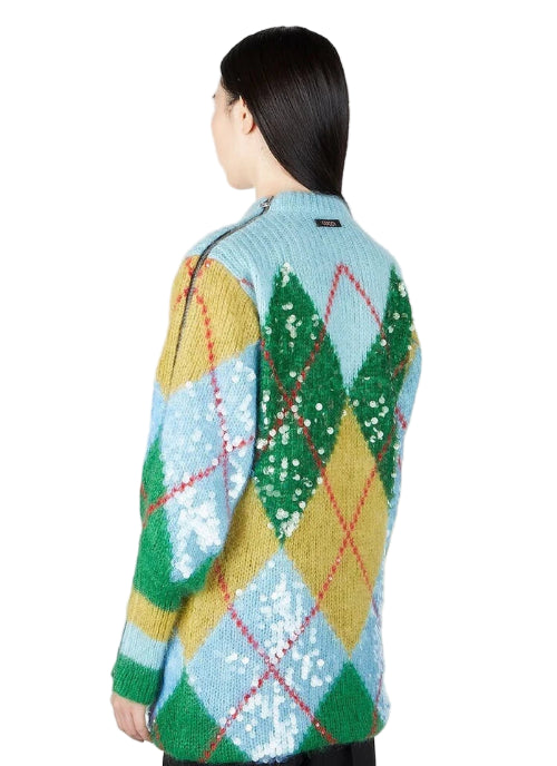Person wearing a colorful argyle patterned sweater with sequins on a plain background