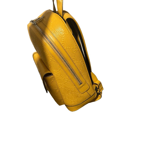 Yellow embossed handbag on a black and white cube against a neutral wall.