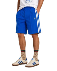 Person wearing blue Adidas shorts with white stripes, Gucci socks, and white sneakers on a plain background