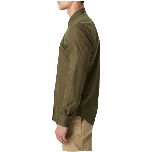 A man shown in side profile wearing an olive green long-sleeve button-up shirt and khaki pants against a light gray studio background.