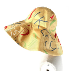 A gold-colored sun hat with a colorful abstract pattern of red, green, and black shapes, displayed on a white mannequin head against a white background.
