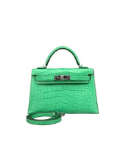 A bright green crocodile-embossed leather handbag with a top handle and a matching detachable shoulder strap, photographed against a neutral gray background.
