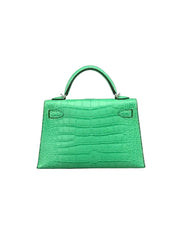 A bright green crocodile-embossed leather handbag with a top handle, photographed against a neutral gray background.