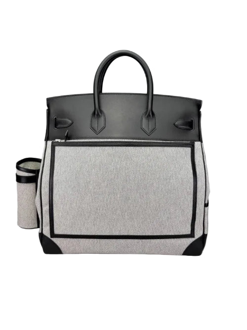 A structured tote bag with a light gray heathered front panel, black leather top and handles, and black trim, shown on a neutral gray background. A matching insulated cup is partially visible to the left.