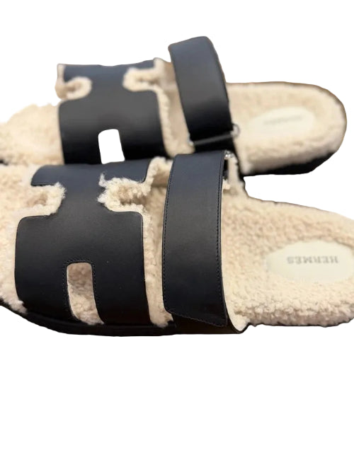 Beige slippers with black straps on a wooden surface