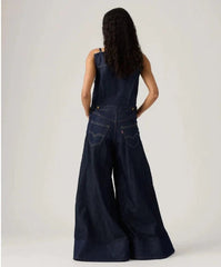 Person wearing a dark blue denim jumpsuit on a plain background