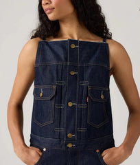 Woman wearing a denim sleeveless top with gold buttons on a plain background