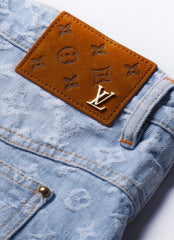 Close-up of light blue monogram denim jeans with a brown leather patch featuring embossed Louis Vuitton monogram motifs and a gold-tone LV logo.