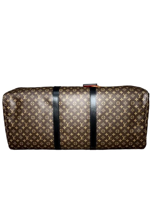 A Louis Vuitton monogram canvas duffel bag with black leather straps, resting on a wooden surface against a gray textured background.