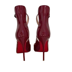 A pair of high-heeled red ankle boots with side cutouts and a glossy finish, standing on a brown cardboard box against a plain light background.