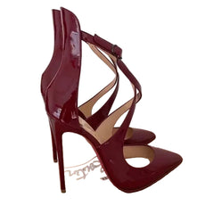 A pair of burgundy patent leather high-heeled sandals with criss-cross ankle straps, shown on a light-colored wooden shoebox.