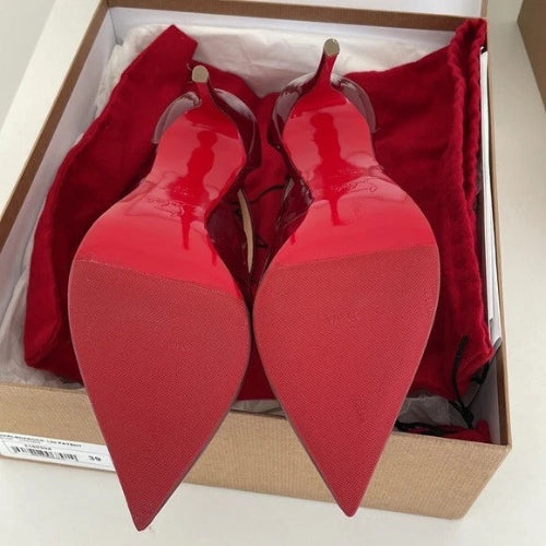 A pair of red patent leather pointed-toe high heels resting in an open shoebox with red dust bags.