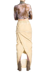 A vintage-style sculpture of a seated female figure wearing a beige sarong and brown leather sandals, shown against a plain white background.