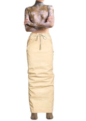 A model wearing a beige drawstring skirt and a brown and beige patterned long-sleeve mock neck top, standing against a light gray studio background.