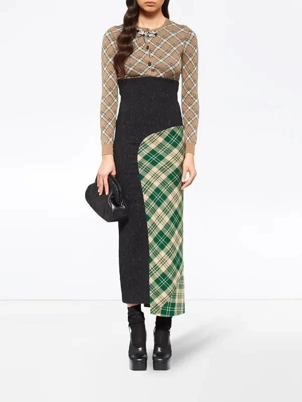 A model wears a long-sleeve midi dress featuring a beige and brown argyle knit top, a black textured waist and skirt, and a green and beige plaid side panel. She is holding a black clutch and wearing black platform ankle boots against a white studio background.