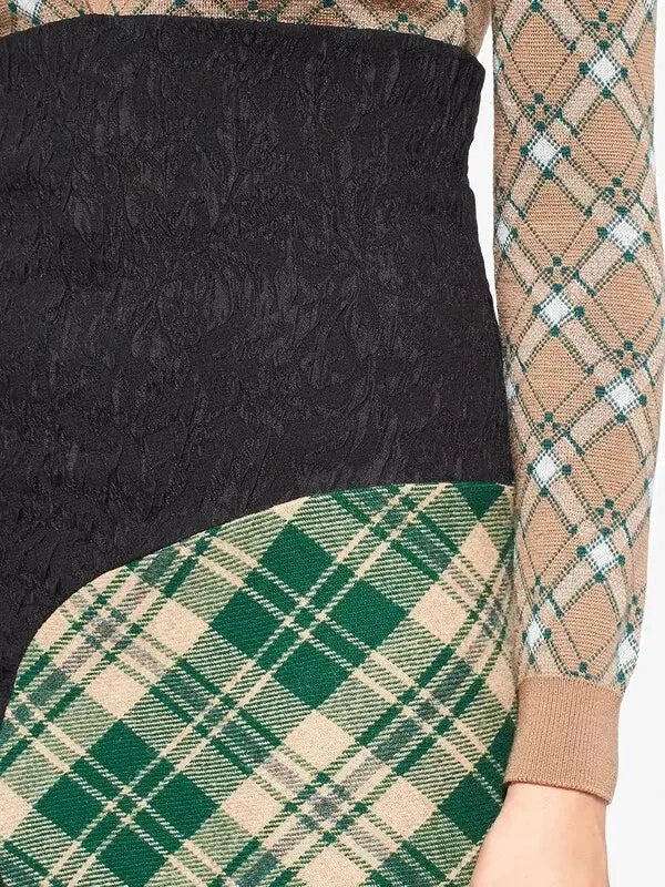Close-up of a long-sleeve knit top with a color-blocked design: black textured lace on the upper section, green and beige tartan plaid on the lower section and left sleeve, and a beige plaid pattern on the right sleeve.