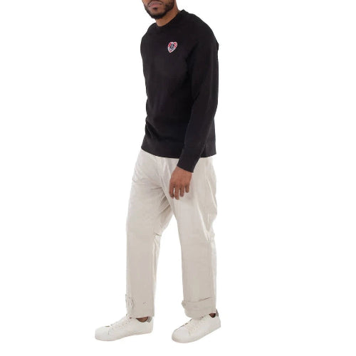 Person wearing a black sweatshirt with a heart design and light-colored pants on a white background