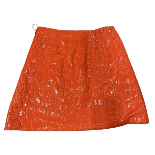 An orange crocodile-embossed faux-leather mini skirt with a glossy finish, shown against a sky and clouds background.
