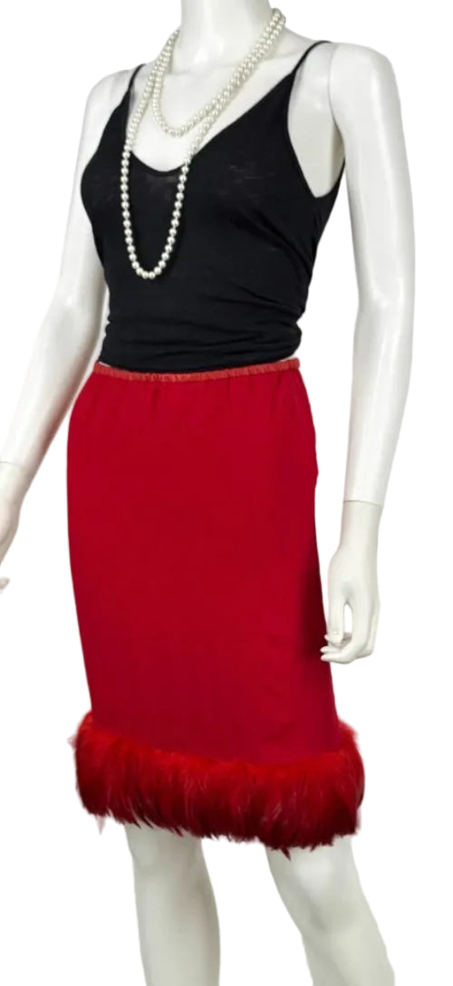 A red pencil skirt with a feather-trimmed hem, styled on a white mannequin with a black camisole top and pearl necklaces.