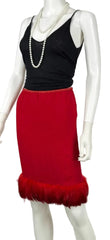 A red pencil skirt with a feather-trimmed hem, styled on a white mannequin with a black camisole top and pearl necklaces.