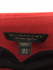 Close-up of a Burberry garment label on a red and black fabric item, with the Burberry London England brand tag and a Made in Italy size tag visible.