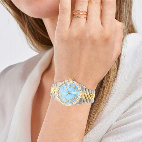 Gold and silver watch with blue face on a wrist against a white background