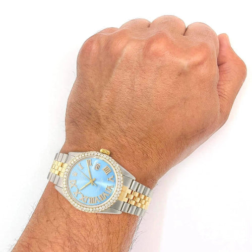 Hand wearing a gold and silver watch with a blue face on a white background