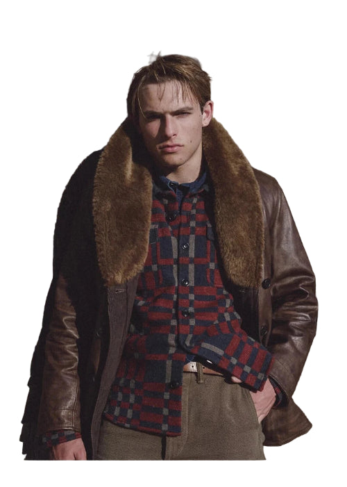 Man wearing a brown leather coat with fur collar against a wooden wall.