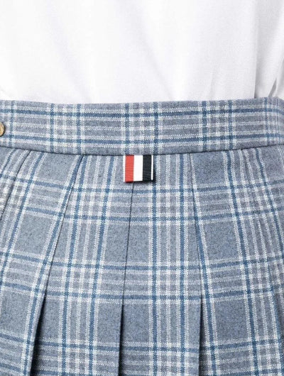 Close-up of a blue and gray plaid pleated skirt with a signature Thomé Wright flag tab at the waistband, worn with a white top.