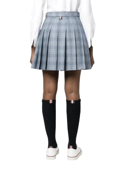 A model from the back wearing a pleated plaid mini skirt in blue and white, paired with a white long-sleeve top, black knee-high socks, and white sneakers.