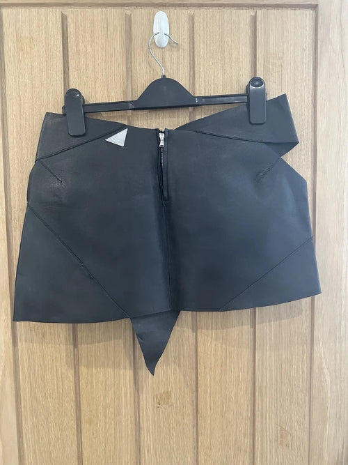 Black leather skirt on a hanger against a wooden panel background