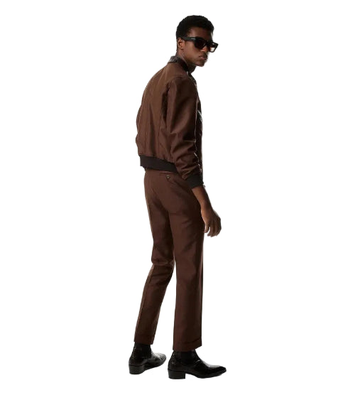 A man wearing a brown tailored jacket and matching trousers with black boots and sunglasses, photographed in profile against a clean white studio background.
