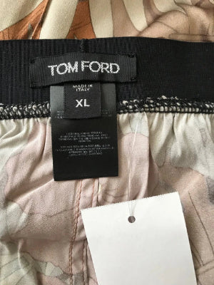 Close-up of the inner waistband of a Tom Ford garment, showing the black brand label, size XL, and a white retail hangtag over a light beige and pink patterned fabric.