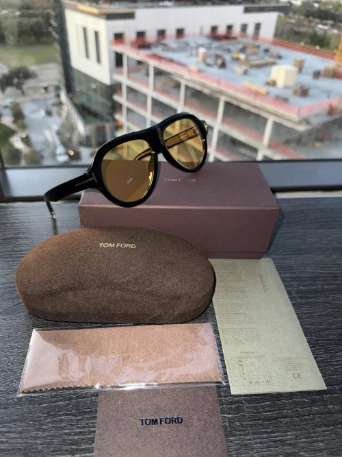 Tom Ford sunglasses with case and box on a reflective surface with a cityscape background