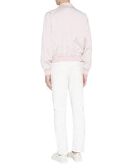 A model shown from the back wearing a light pink satin bomber jacket, white trousers, and white sneakers against a light gray studio background.