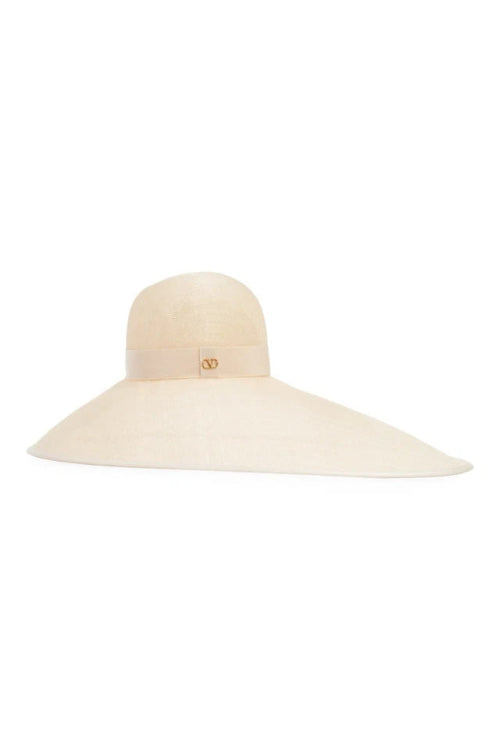A light beige wide-brimmed sun hat with a small gold-tone interlocking V logo on the front band, set against a plain white background.