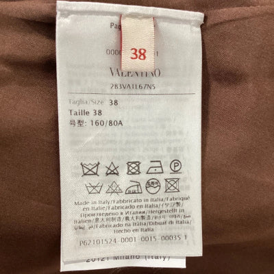 A close-up of a white laundry care label attached to a brown garment, showing the brand name '38' and washing instructions.