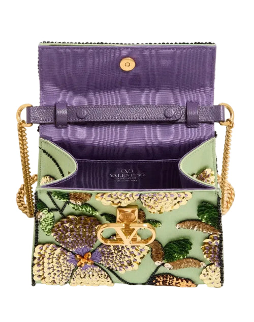 A purple textured leather clutch bag with a gold-tone chain strap and a floral embroidered front pocket featuring green, yellow, and orange details.