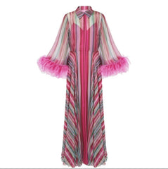 A long-sleeved maxi dress with vertical pink, red, and gray stripes, featuring a high collar and voluminous pink feathered cuffs, shown against a plain white background.